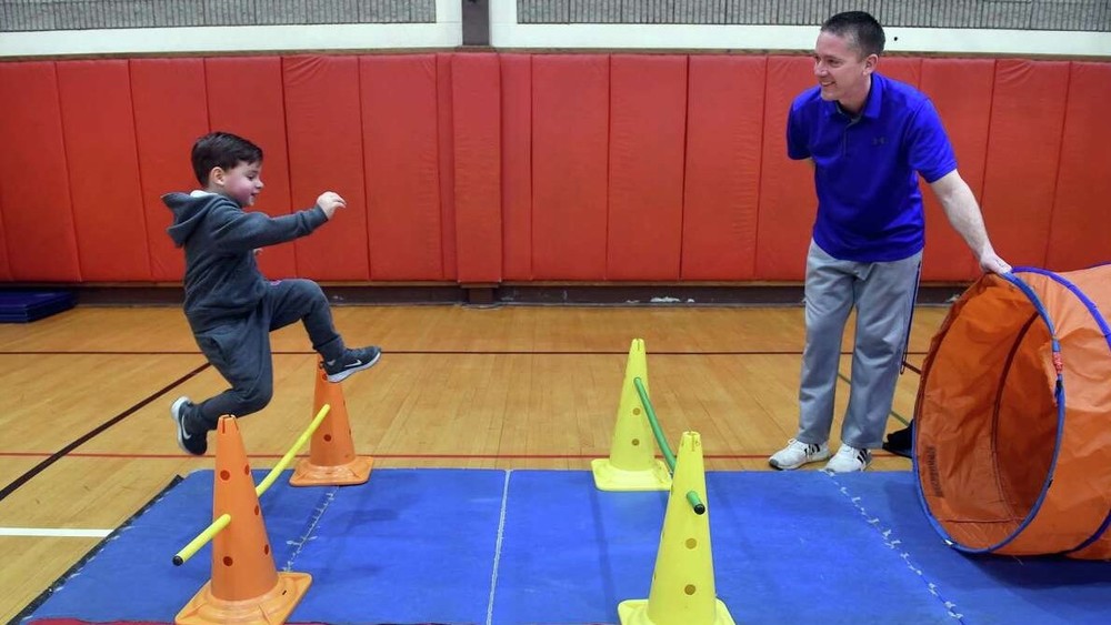 Physical education teacher Glenn Healy watches kindergartner Lucas D'Amato jump over a bar in an obstacle course in the gymnasium at Savin Rock Community School in West Haven.